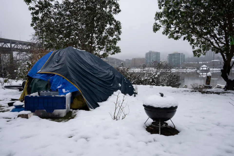 Blue tent with small charcoal grill and plastic bin set up by unhoused person in snow in Portland, Oregon.